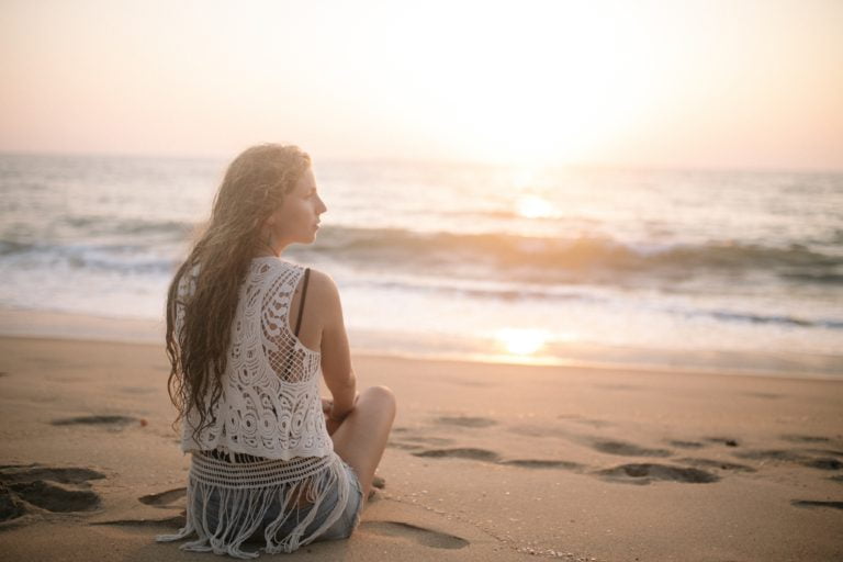Woman sitting on beach at peace during sunset